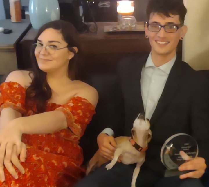 Women in red dress and man in suit holding an award.
