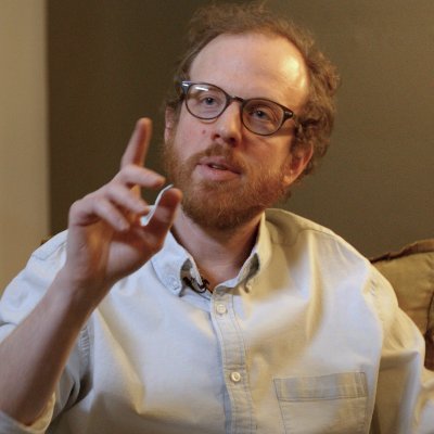 Man in chair with raised hand.